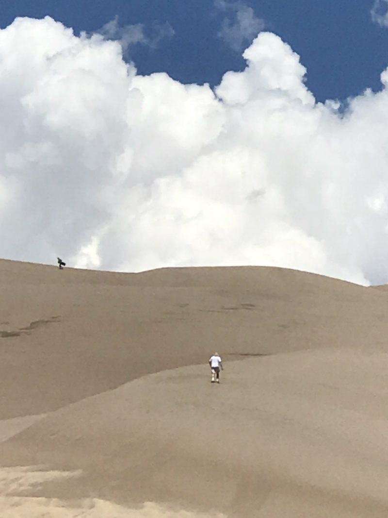 man walking up sand dune